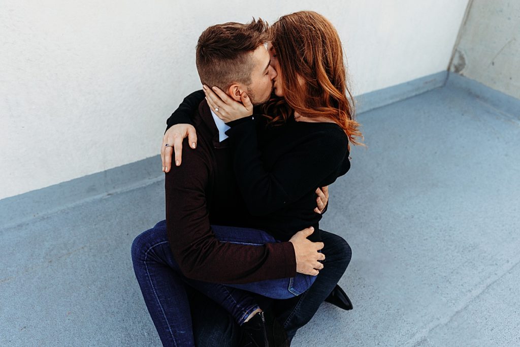 couple sitting on floor kissing on top of parking garage
