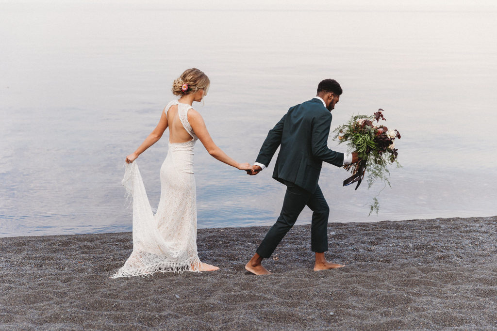 couple holding hands walking on beach at elopement