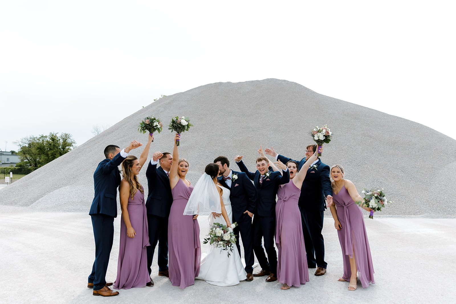 bridal party posing as bride and groom kiss with Michigan wedding photographer Port 393 Wedding In Holland, Michigan | Allie + Ryan
