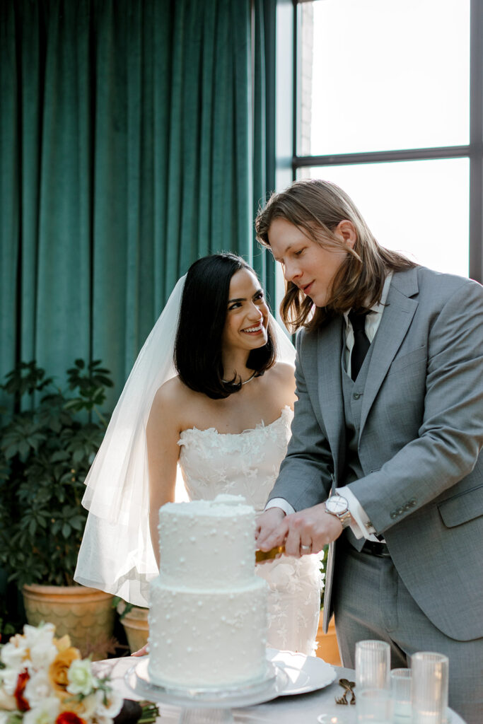 Bride smiles at groom as he cuts their cake at their mocha-themed wedding