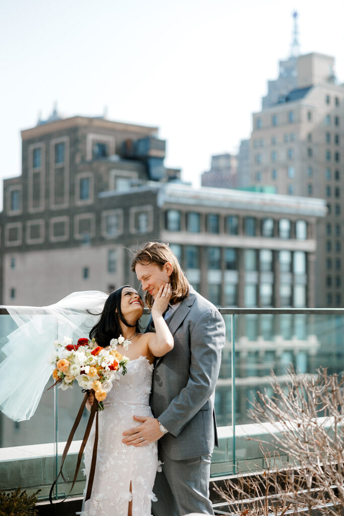 Groom looks down at bride lovingly as they stand on rooftop of Book Tower in downtown Detroit