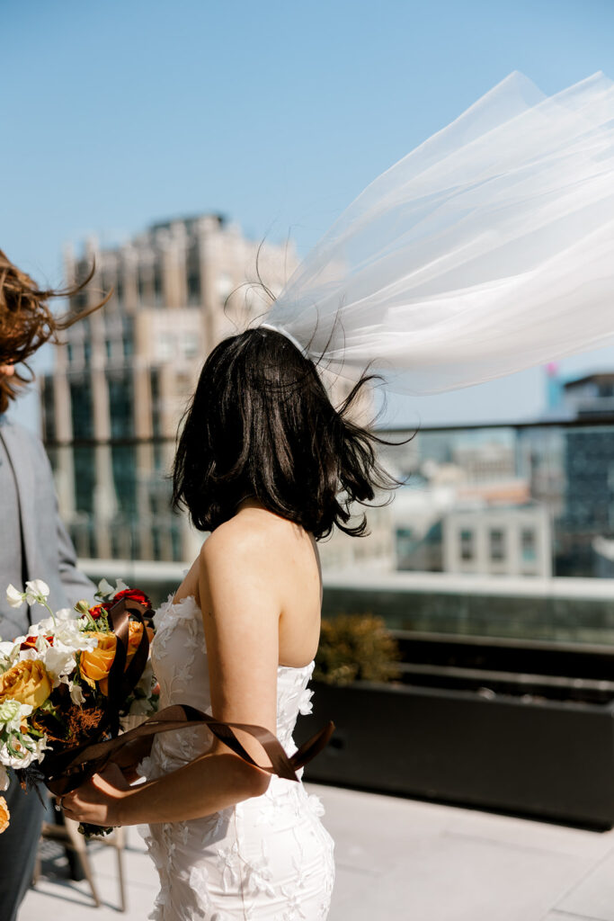 Bride's veil whips in the wind as she stands on Book Tower rooftop overlooking the downtown Detroit cityscape