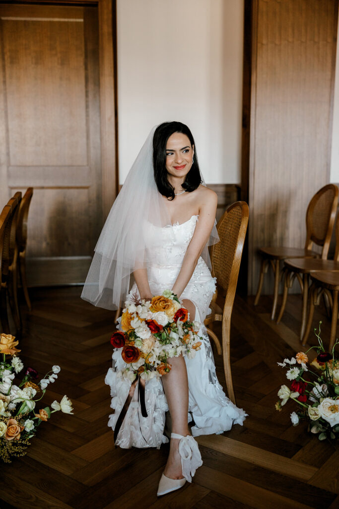 Bride sits on cane back chair holding her vibrant florals