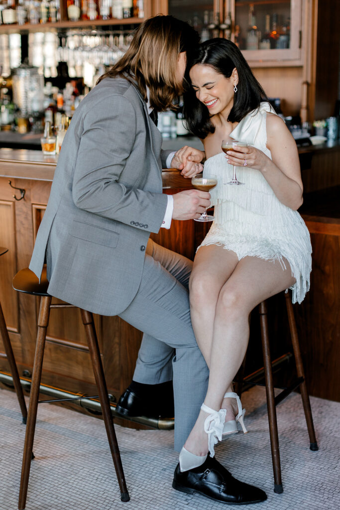 Bride laughs as groom whispers something in her ear at bar at Book Tower in downtown Detroit