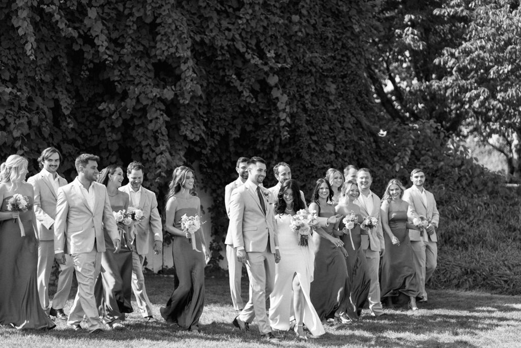 Massive wedding party walks across the lawn in editorial style candids at Michigan wedding