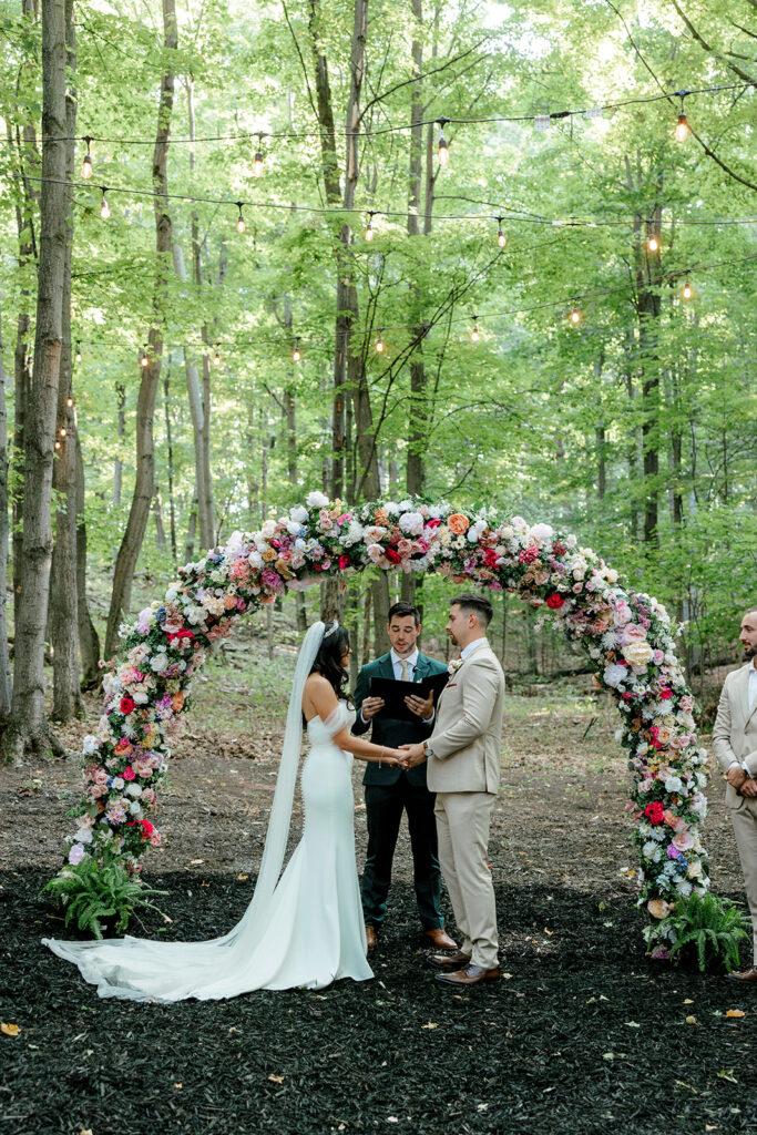 Bride and groom stand under brightly colored floral arch for their Michigan wedding ceremony