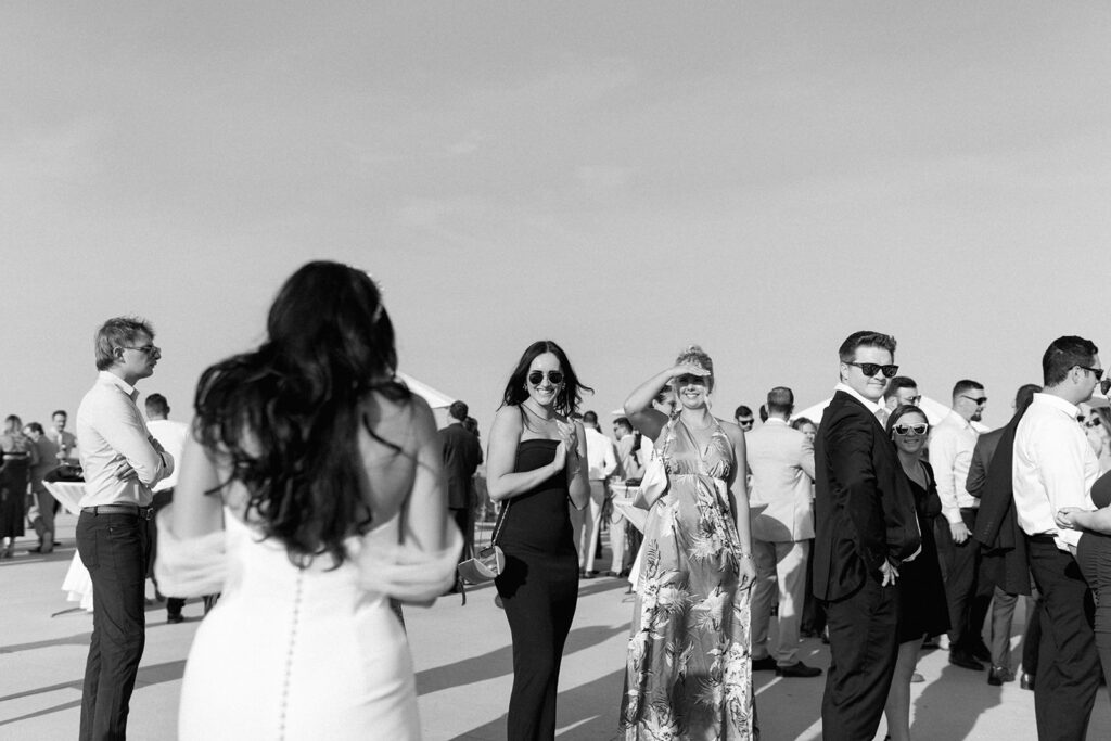 Wedding guests exclaim with excitement as bride approaches them at sunlit cocktail hour.