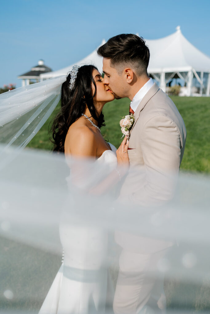 Bride and groom kiss under cloudless sky outside tented reception