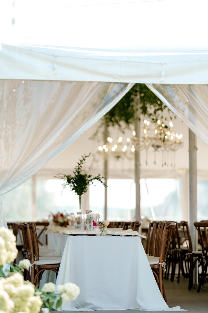 Gorgeous tented reception with wooden chairs and lush greenery adorning the chandeliers
