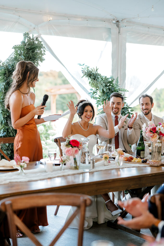 Bride and groom cheer and clap during maid of honor's speech