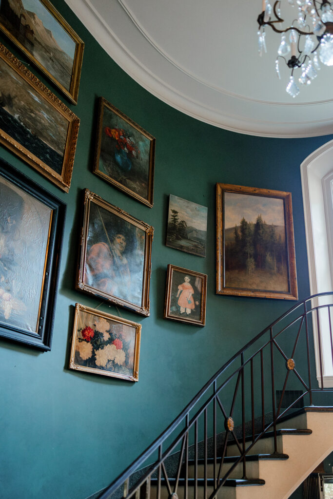 Manor staircase with rich teal walls and historical French artwork