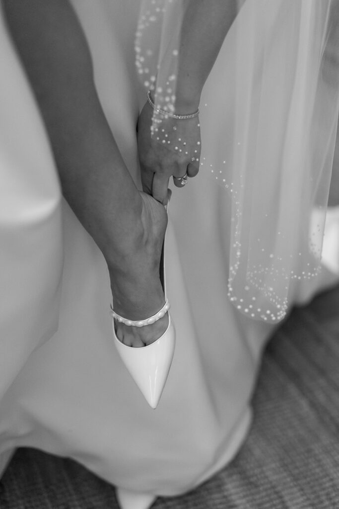 Close-up of bride holding her pearl-detailed shoes, a wedding detail photo with classic elegance.