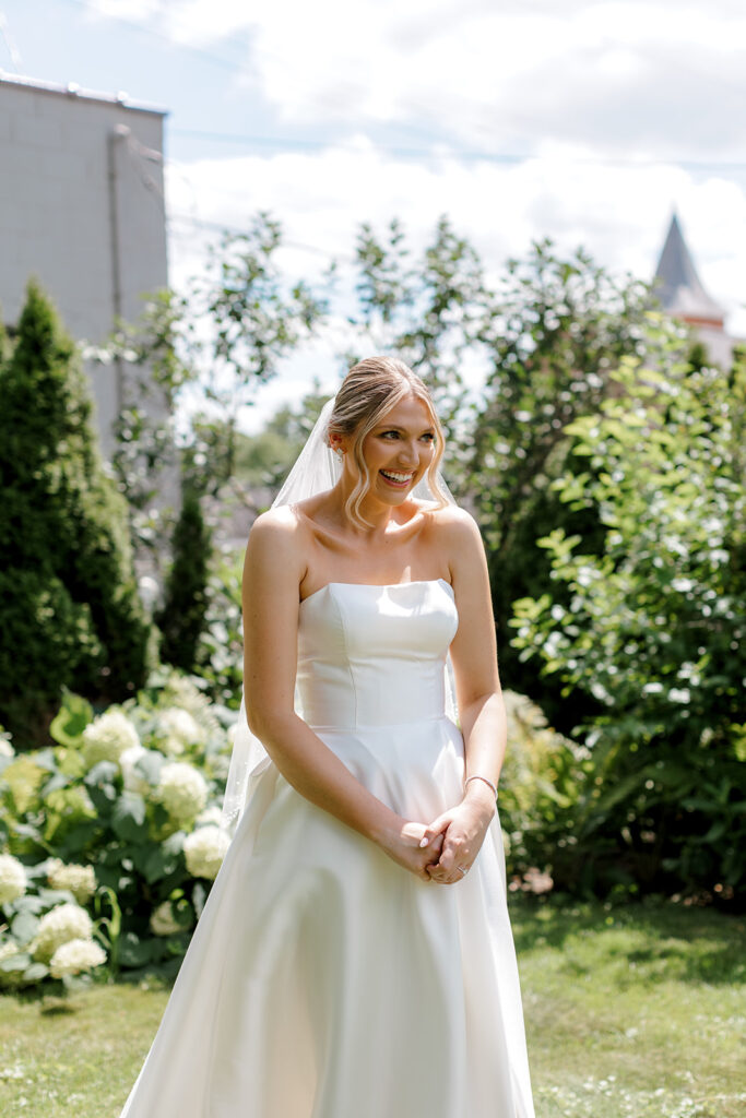 Bride smiling shyly during first look anticipation, a sweet emotional beat before vows are shared.