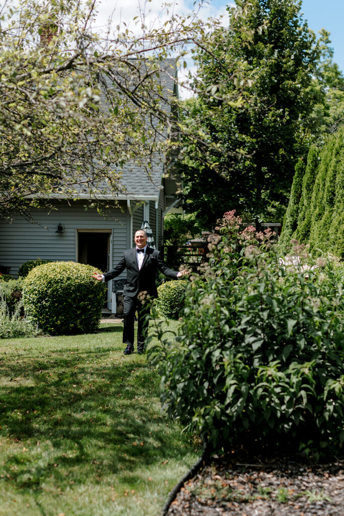 Bride’s brother walking toward her for a surprise first look moment, framed by blooming Michigan garden landscape.