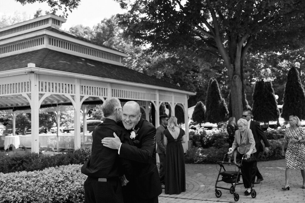 Guests greeting each other and hugging under gazebo, authentic pre-ceremony candids.