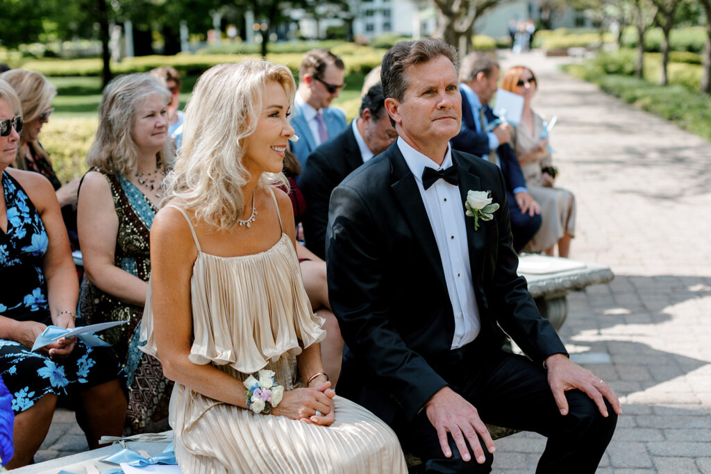 Parents seated during outdoor ceremony, their reactions a reminder of legacy and love.