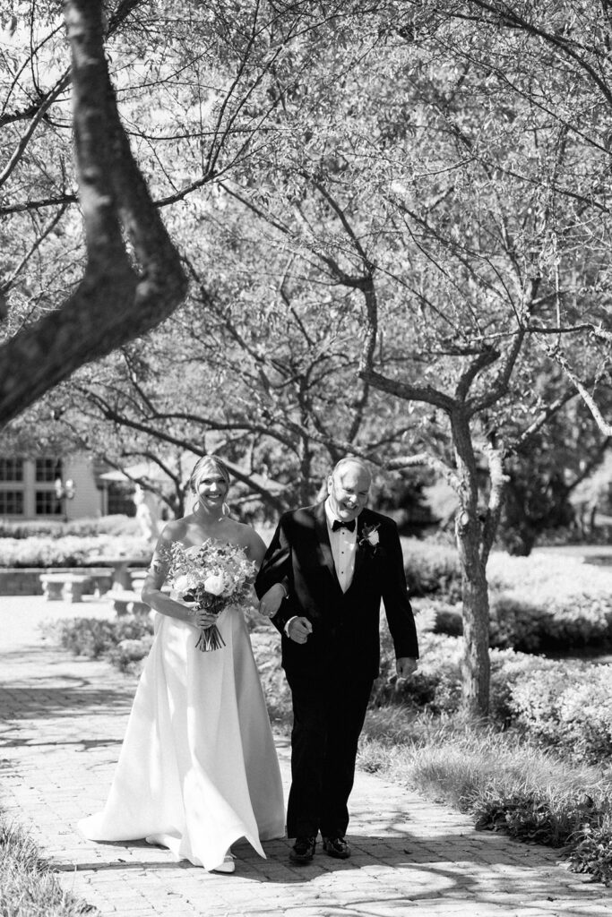 Bride walking down the aisle with her father under dappled orchard light, an emotional walk to remember.