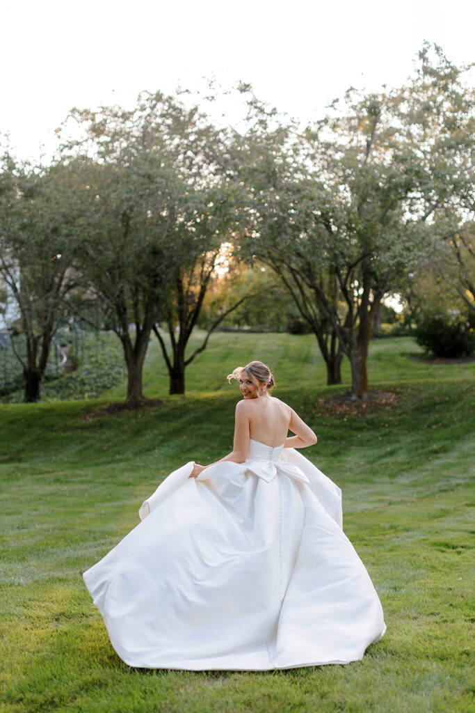 Bride twirling in her gown under the orchard trees, a joyful candid photo showcasing personal style and emotion.