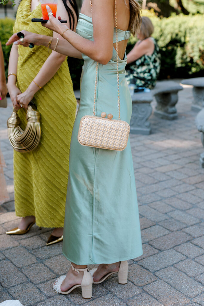 Group of guests in pastel dresses with woven bags and gold accessories, showcasing candid fashion-forward wedding guest moments.