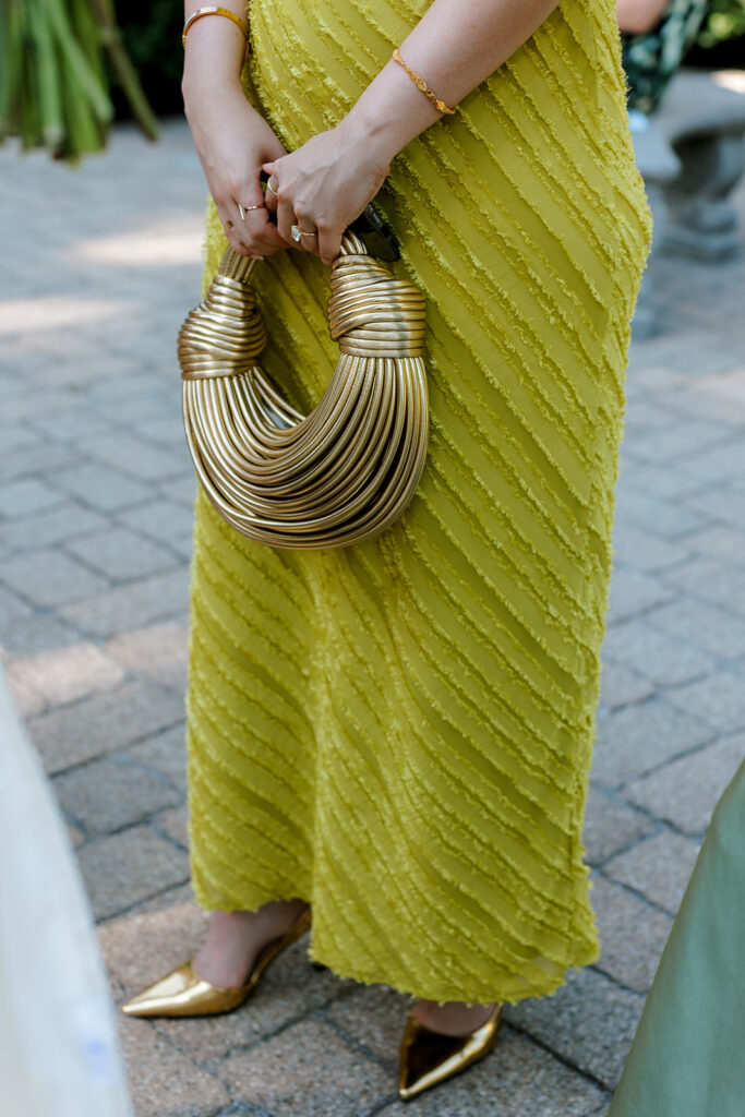 Close-up of guest holding a sculptural gold handbag, a modern style moment to include on a creative wedding shot list.