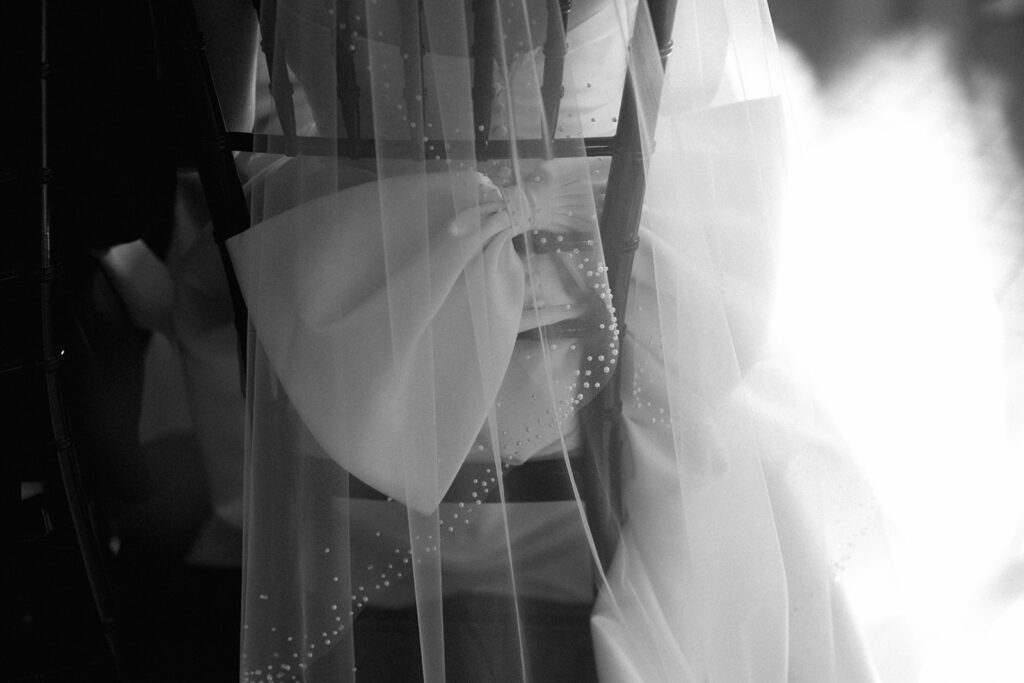Black and white image of veil draped over gown’s oversized bow, an editorial-style dress detail photo.
