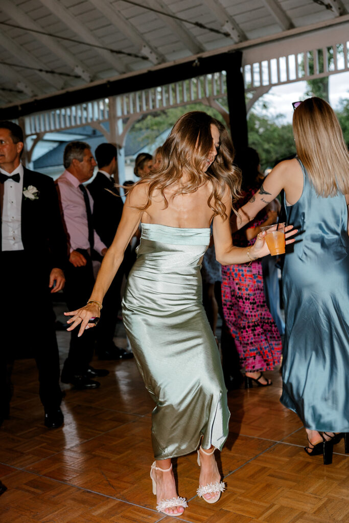 Guest in satin green dress dancing during reception, capturing wedding celebration in motion.