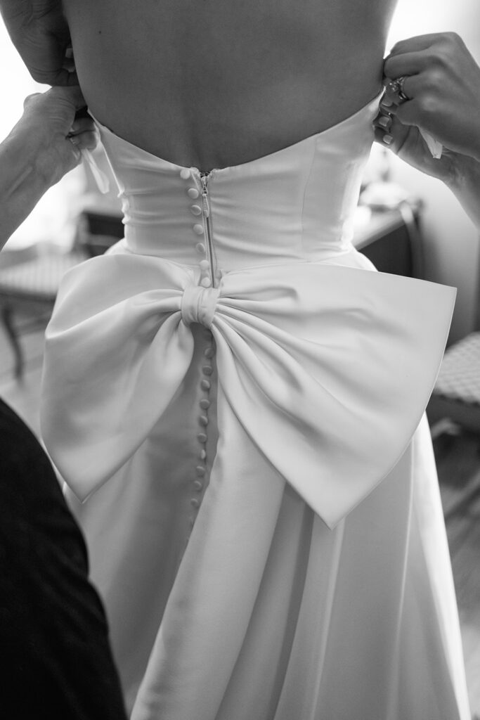 Close-up of the back of bride’s gown featuring sculptural bow and fabric buttons, a fashion-forward wedding detail photo.